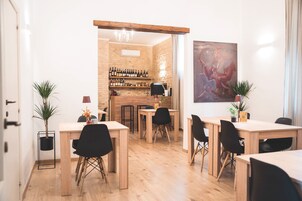 Un comedor con mesas y sillas de madera, una barra con botellas de vino y un gran cuadro abstracto en la pared.