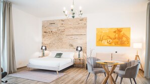 Ein modernes Schlafzimmer mit einem großen Bett, einer Kandelaberleuchte, einem Esstisch mit Stühlen und einem Gemälde an der Wand.