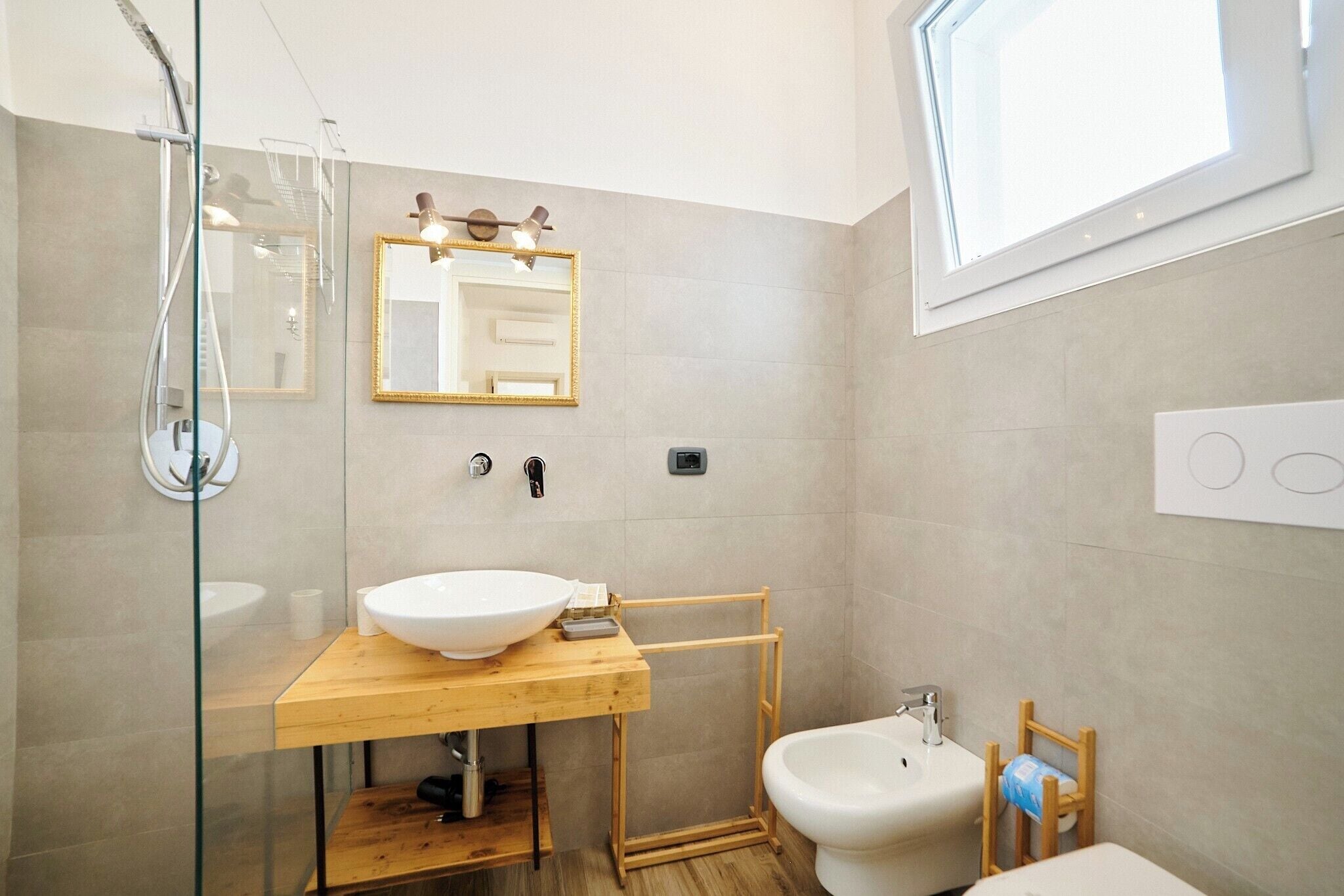 A modern bathroom with a glass-enclosed shower, a wooden vanity with a large sink, a mirror, and a toilet.