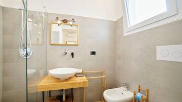 A modern bathroom with a glass-enclosed shower, a wooden vanity with a large sink, a mirror, and a toilet.