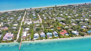 An aerial view of a coastal residential area with houses, a pier, and a beach.