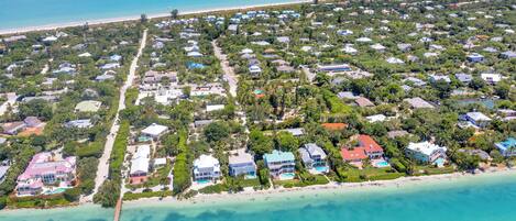 An aerial view of a coastal residential area with houses, a pier, and a beach.