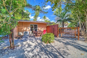 A small building with a covered patio, a wooden fence, and a gravel driveway.