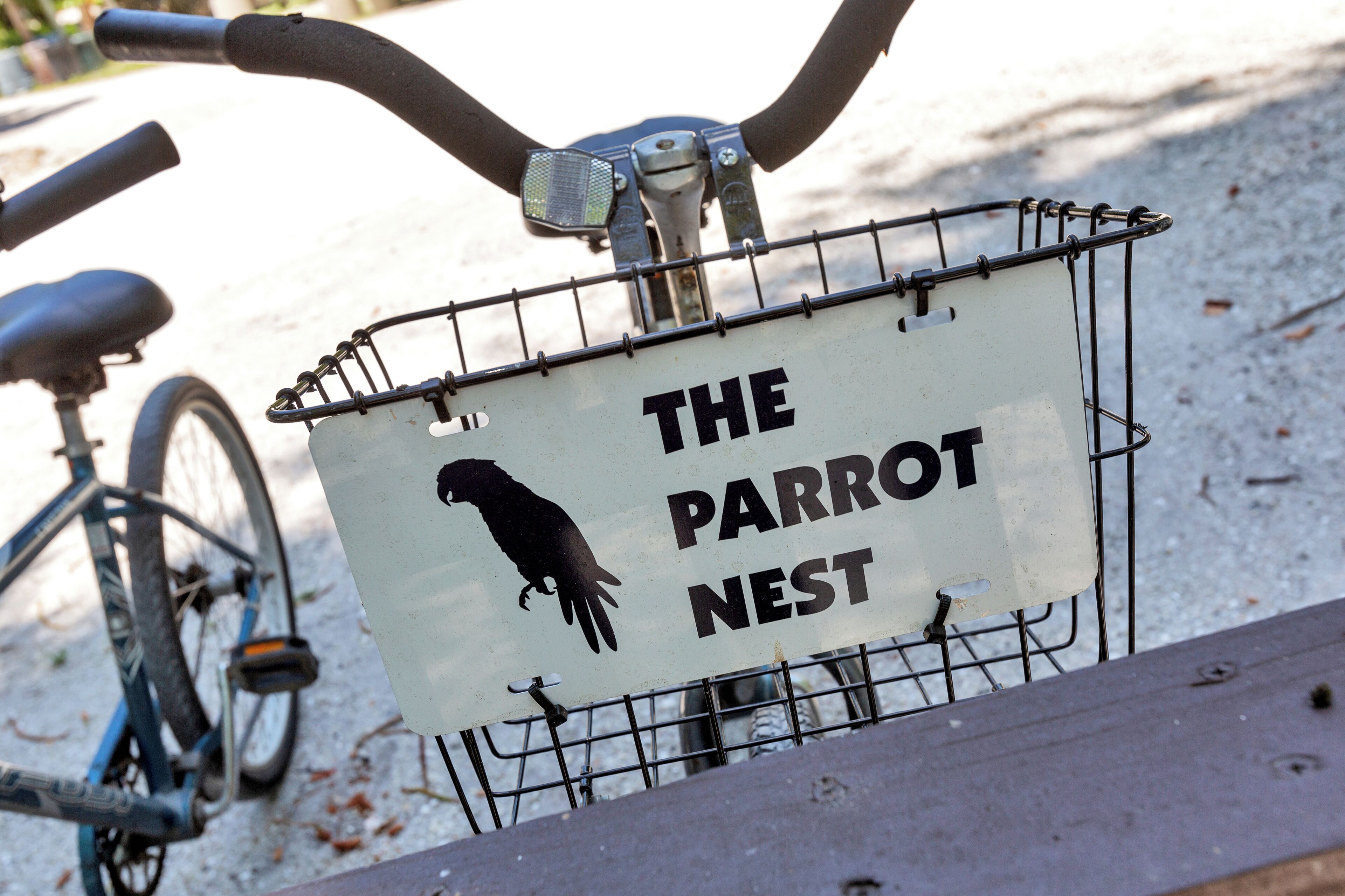 A bicycle with a basket containing a sign that reads "THE PARROT NEST".