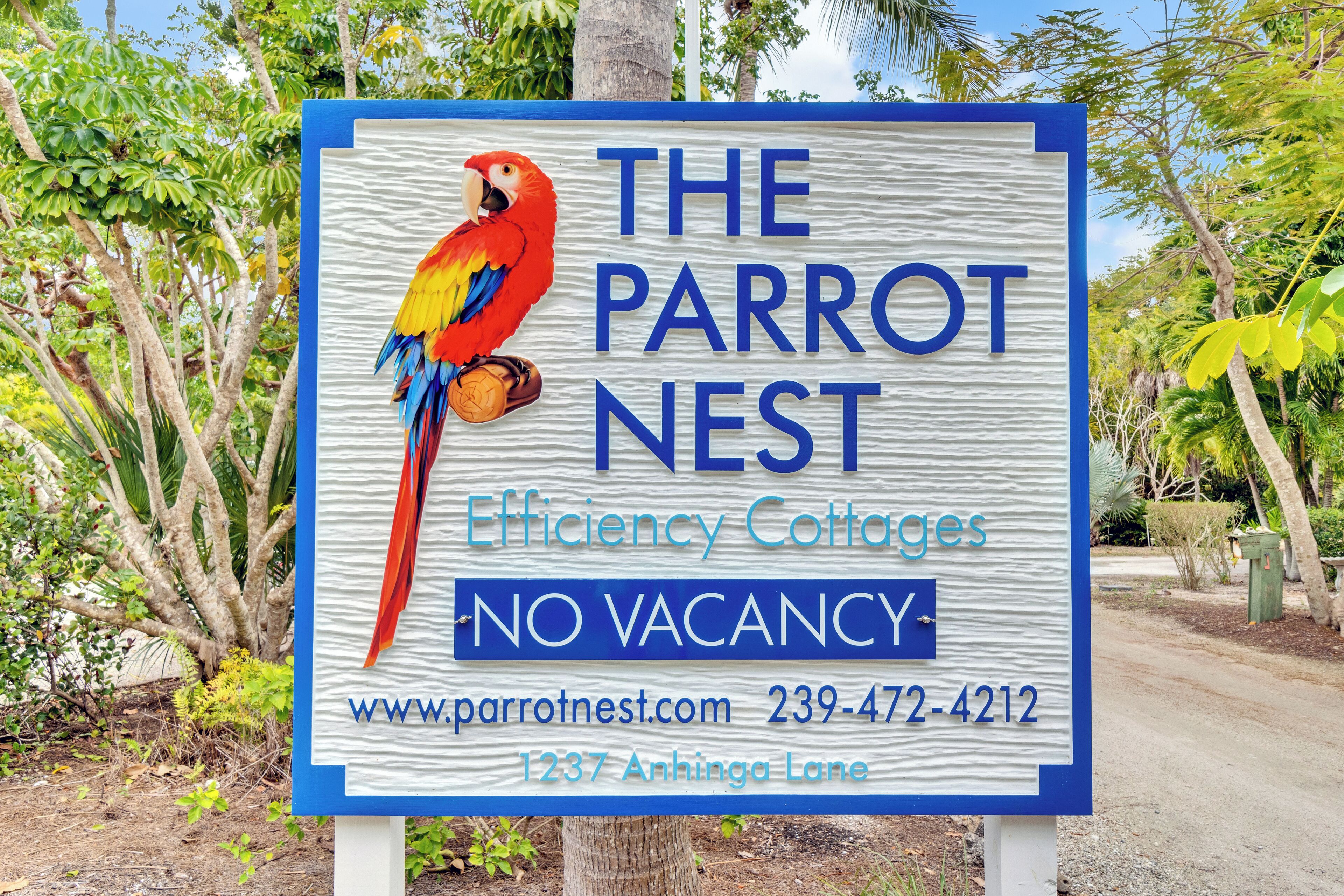 Placa para 'The Parrot Nest Efficiency Cottages' com ilustração de um papagaio, indicando 'SEM VAGAS' e exibindo um site e número de telefone.