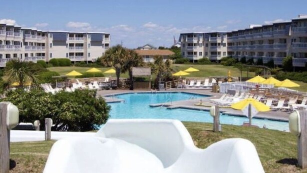 A pool area with lounge chairs and umbrellas, surrounded by multi-story buildings. - A Place at the Beach resort Family Fun!150'Waterslide, indoor pool&Putt Putt (Atlantic Beach)