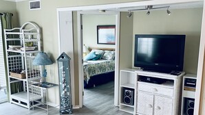 A living room with a television, wicker furniture, and a bookshelf. - A Place at the Beach resort Family Fun!150'Waterslide, indoor pool&Putt Putt (Atlantic Beach)