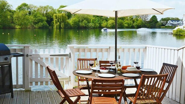 Een terras met een eettafel, met uitzicht op een meer en een boot in de verte.
