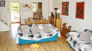 Een ruime woonkamer met een blauwe bank, een houten eettafel en een keuken op de achtergrond.