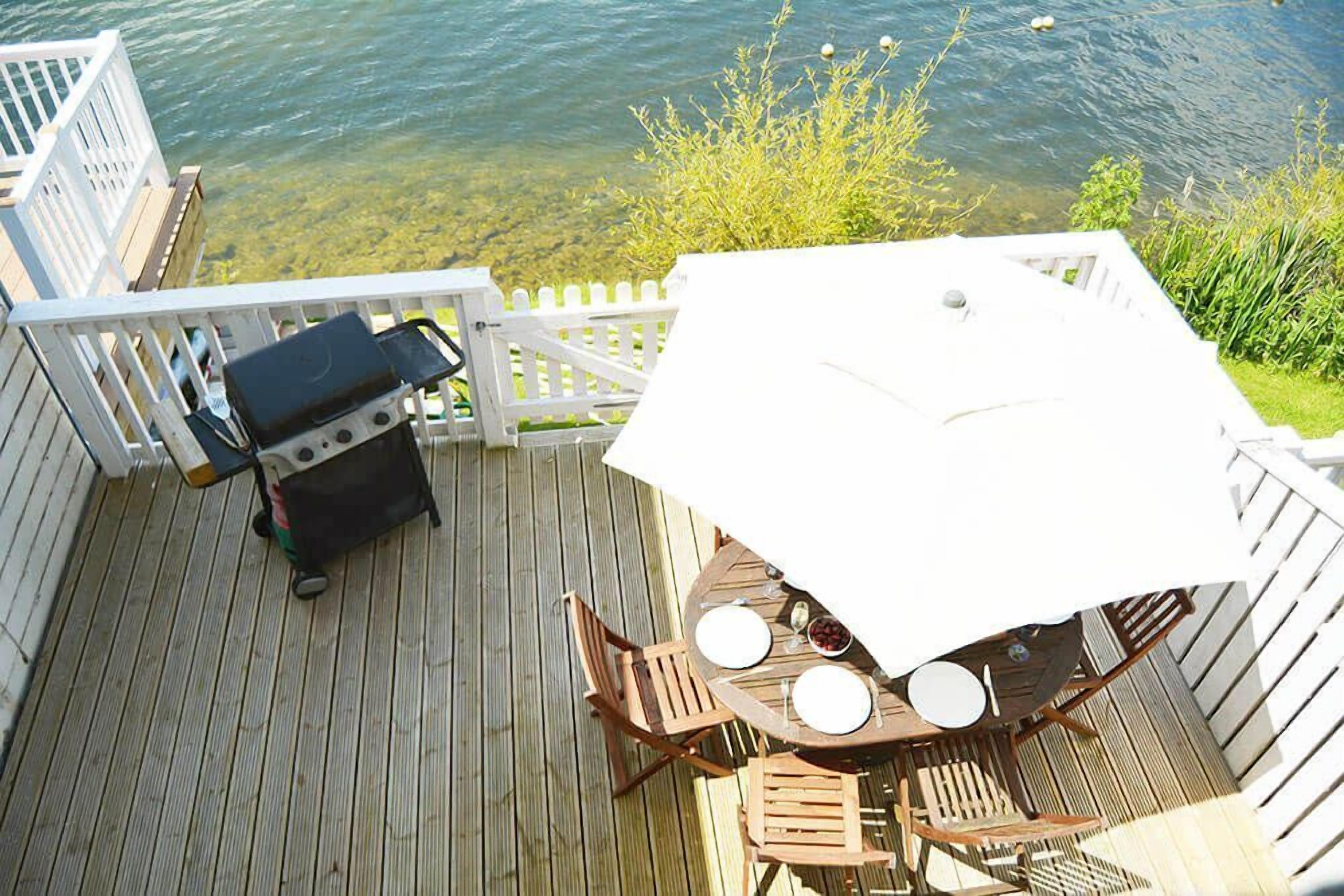 Een houten terras met een tafel, stoelen, een barbecue en uitzicht op een meer.