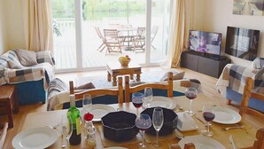 Een eethoek met een tafel voor vier personen, een televisie en uitzicht op een terras en water.