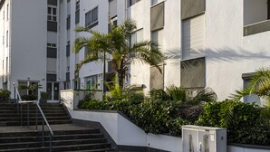 Ein mehrstöckiges Gebäude mit weißer Fassade, einer Treppe im Freien und einer kleinen Gartenanlage mit Palmen.