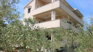 Um edifício de vários andares com varandas, rodeado por oliveiras.