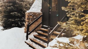 A wooden cabin with a stone staircase leading to a door, surrounded by snow and trees. - The Fox A-Frame | An Intimate Mountain Retreat (Blue River)