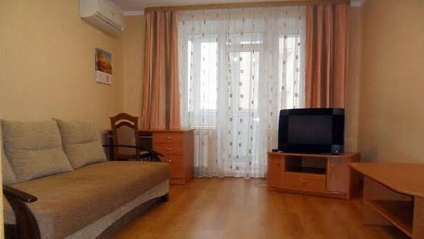 A small, cozy room with a sofa, a TV on a wooden stand, and a desk.