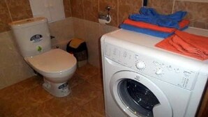 A small laundry room with a washing machine, a toilet, and a cabinet.