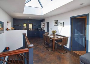 A modern kitchen with dark blue cabinets, a dining area with a wooden table and chairs, and a skylight above the kitchen. - Host & Stay | The Nook (Saltburn-by-the-Sea)