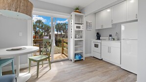 Una cocina moderna con armarios blancos, un comedor con mesa y sillas, y vista a palmeras al exterior.