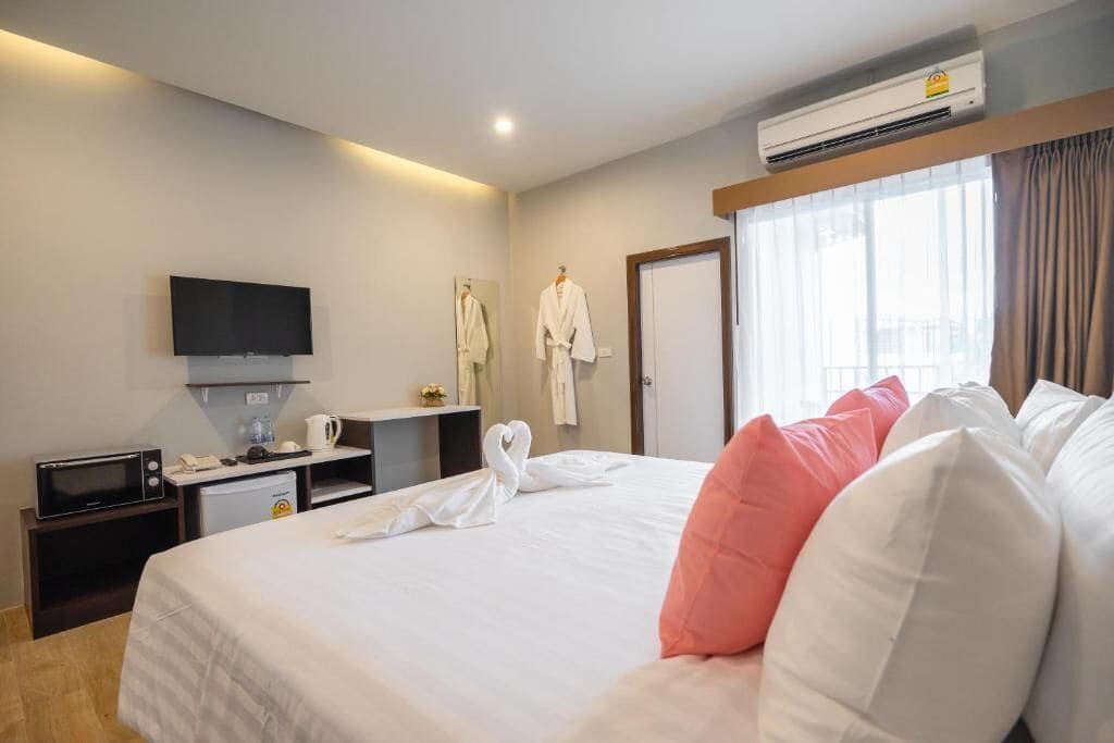 A hotel room with a bed, a flat-screen TV, a mini-fridge, a microwave, a coffee maker, and a window with curtains.