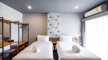 Habitación de hotel con dos camas, un armario de madera, un espejo, un aire acondicionado instalado en la pared y una ventana con cortinas.