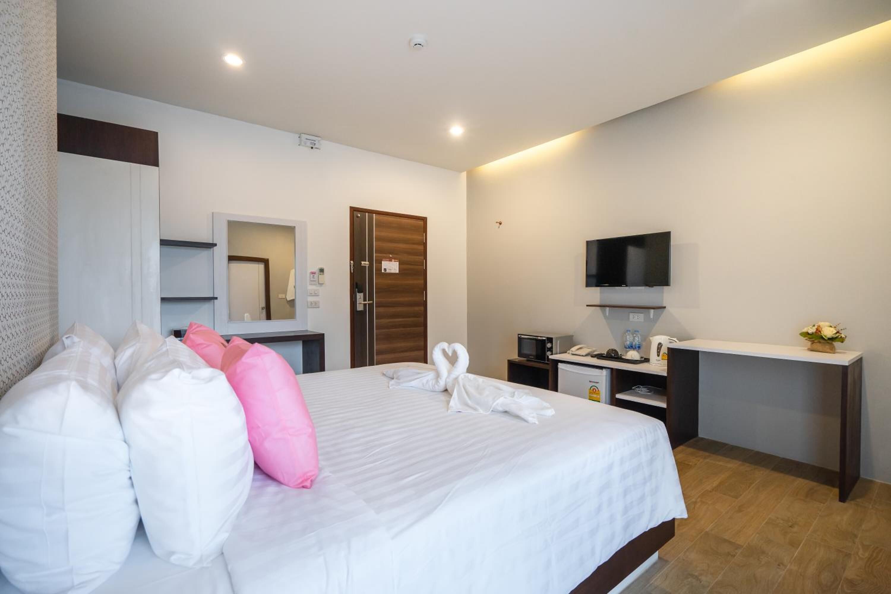 A hotel room with a bed, pillows, a desk with a TV, a microwave, and a small kitchenette.