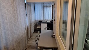 Ein schmaler Flur führt zu einem Essbereich mit Tisch und Stühlen, einer Küchenzeile mit Arbeitsplatte und Schränken sowie einem großen Fenster mit Aussicht.