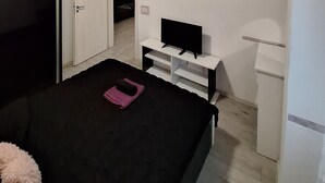 Ein Schlafzimmer mit einem Bett, einem Fernseher auf einem Schrank, einem Kleiderschrank und einer Tür zu einem anderen Raum.