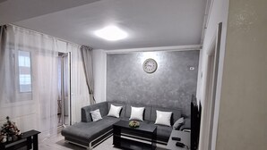 Ein Wohnzimmer mit Ecksofa, Couchtisch, TV-Schrank und Wanduhr.