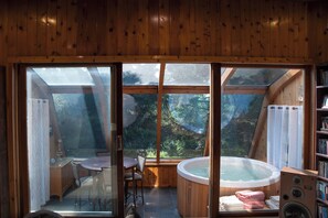 Uma cabana de madeira com uma grande janela de vidro, banheira de hidromassagem, mesa de jantar e cadeiras.