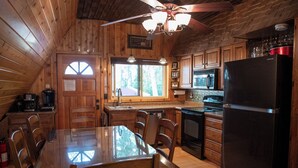 A wooden cabin kitchen with a dining table, chairs, a refrigerator, a microwave, and a ceiling fan.