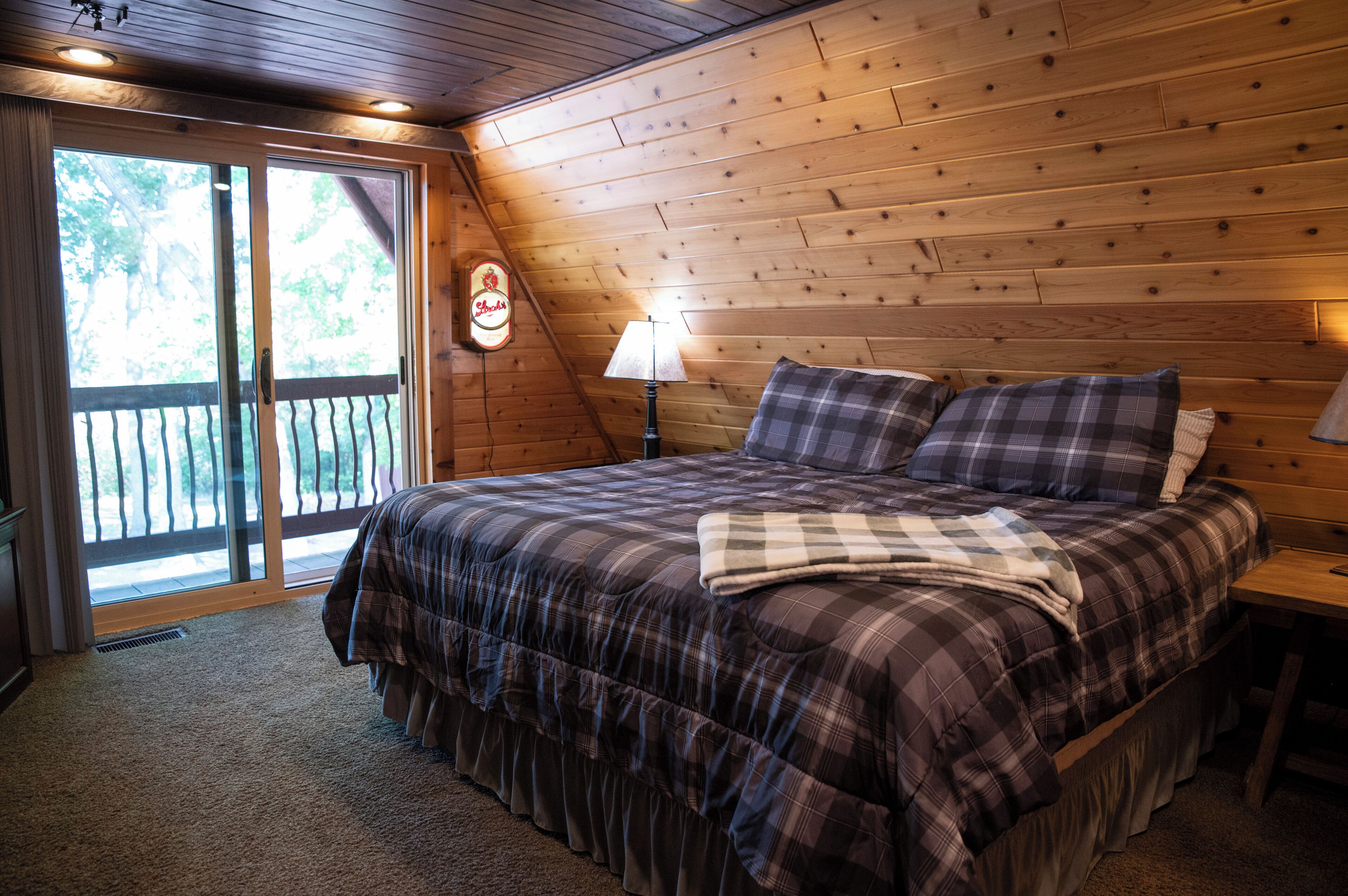 Une chambre avec un grand lit, un plafond en bois et une vue sur l’extérieur, accessible par une porte-fenêtre coulissante.
