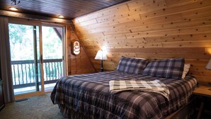 A bedroom with a large bed, a wooden ceiling, and a view through a sliding glass door.