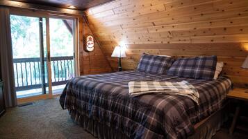 Une chambre avec un grand lit, un plafond en bois et une vue sur l’extérieur, accessible par une porte-fenêtre coulissante.