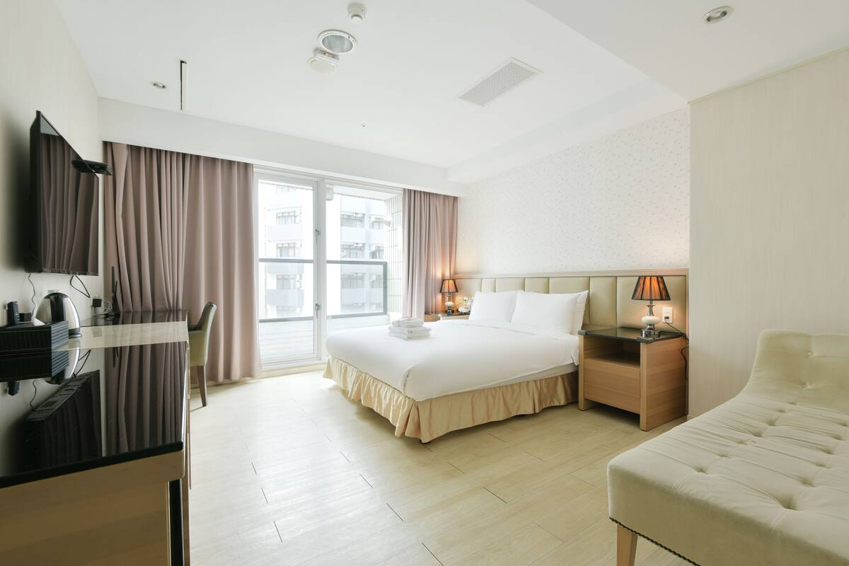 Habitación de hotel con cama, mesita de noche, lámpara y escritorio con computadora.