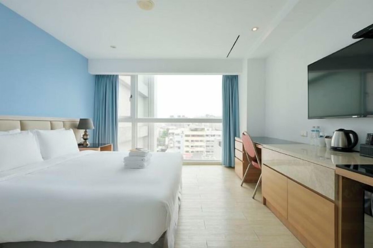 Habitación de hotel con una cama grande, un escritorio, un televisor de pantalla plana y vistas a la ciudad.