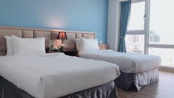 A hotel room with two beds, a nightstand with a lamp, and a large window with curtains.