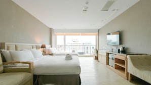 A hotel room with a large bed, a sofa, a TV, and a balcony with a view.