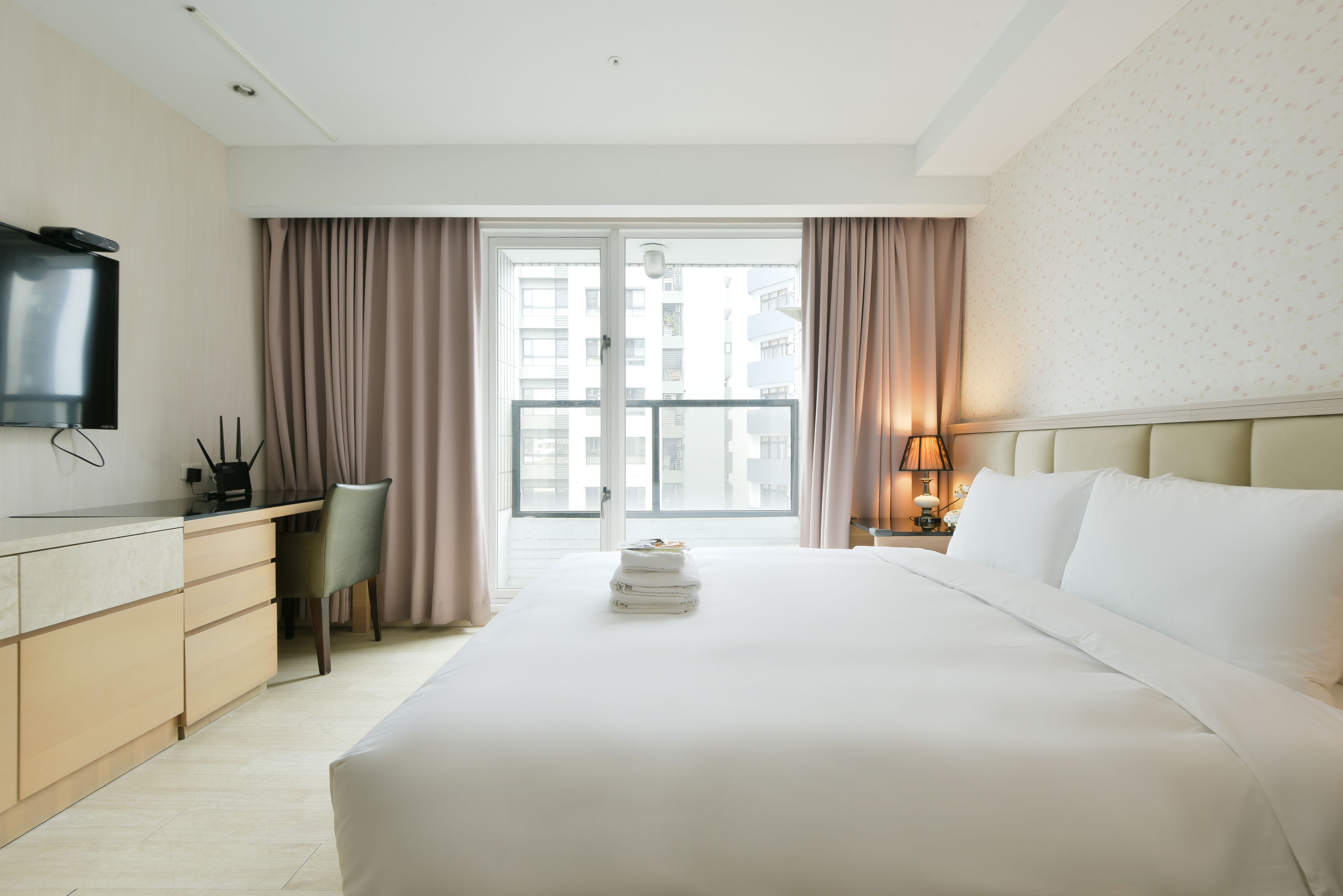 A hotel room with a bed, a desk, a chair, a TV, and a window with curtains.