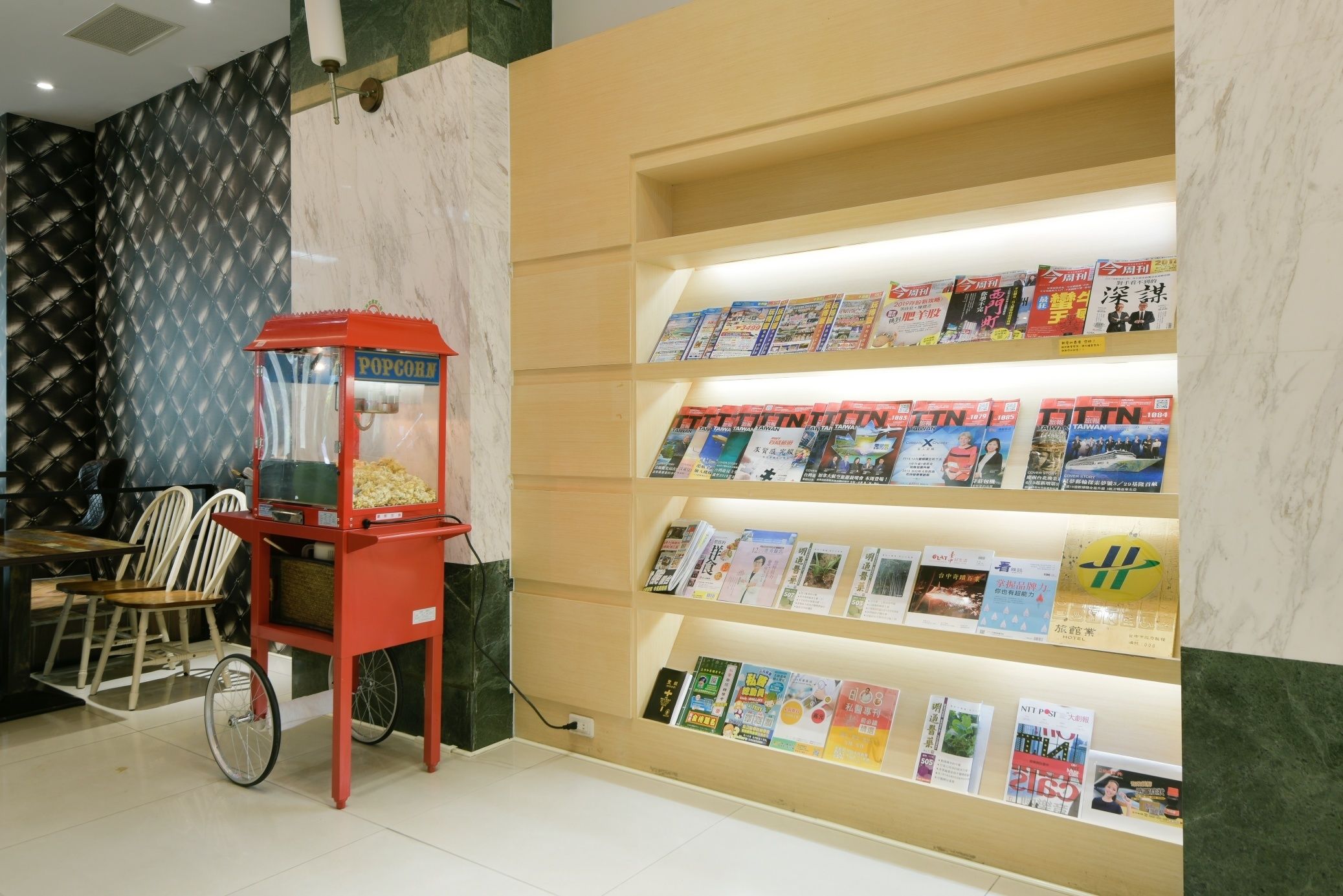 A kiosk with a popcorn machine, a wheelchair, and a wall with bookshelves.
