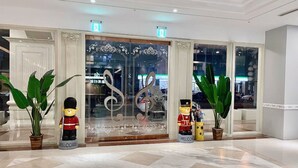 A lobby with a marble floor, a glass door with a decorative metal frame, and two potted plants.