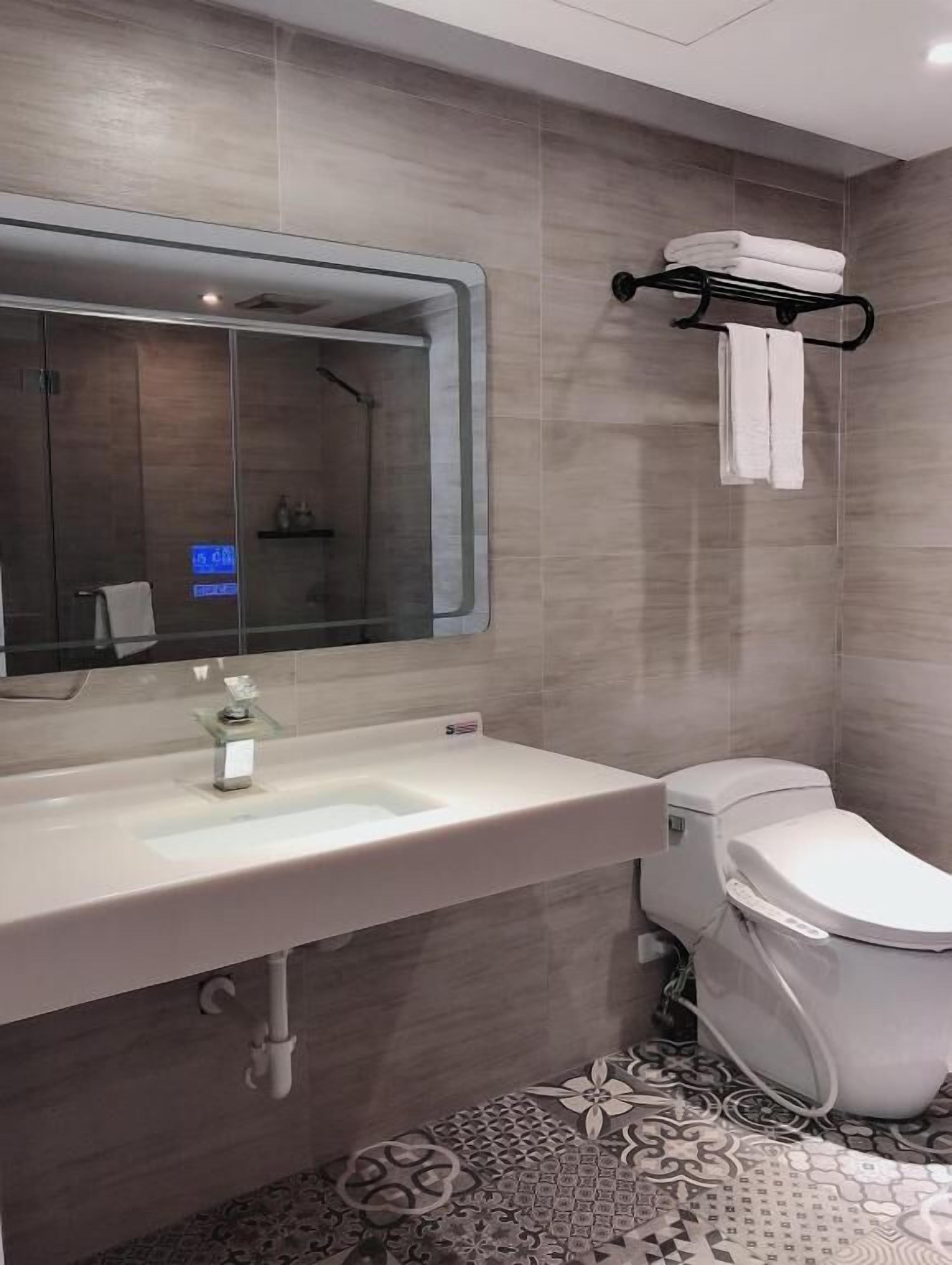 A modern bathroom with a large mirror, a white sink, and a toilet.