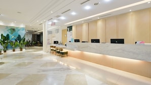 A modern reception area with a marble reception desk, seating, and a large potted plant.