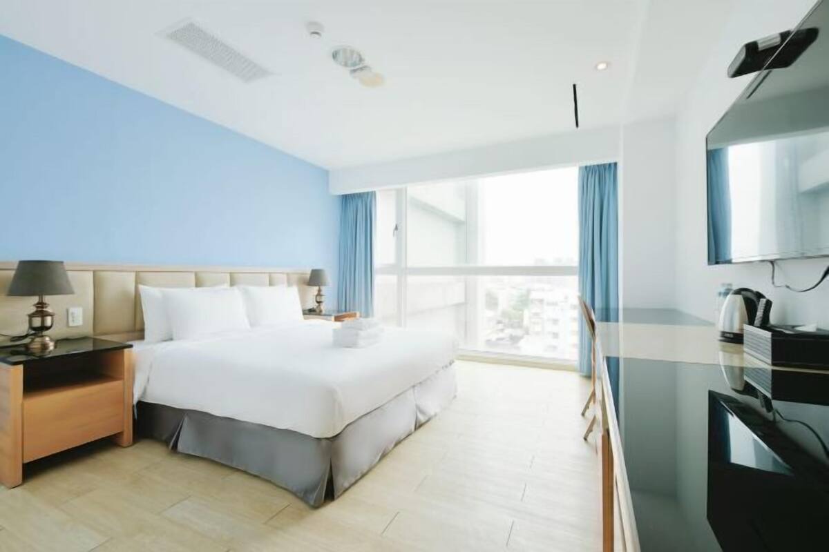 Una habitación de hotel con cama, mesita de noche, lámpara, televisor y vistas a la ciudad.