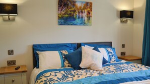Ein ordentlich bezogenes Bett mit blauer und weißer Bettwäsche, ein Gemälde eines Wasserfalls an der Wand und zwei Wandleuchten.