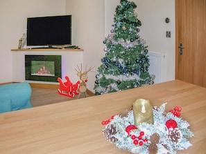 A living room with a fireplace, a television, a Christmas tree, and a table with a candle and decorations.