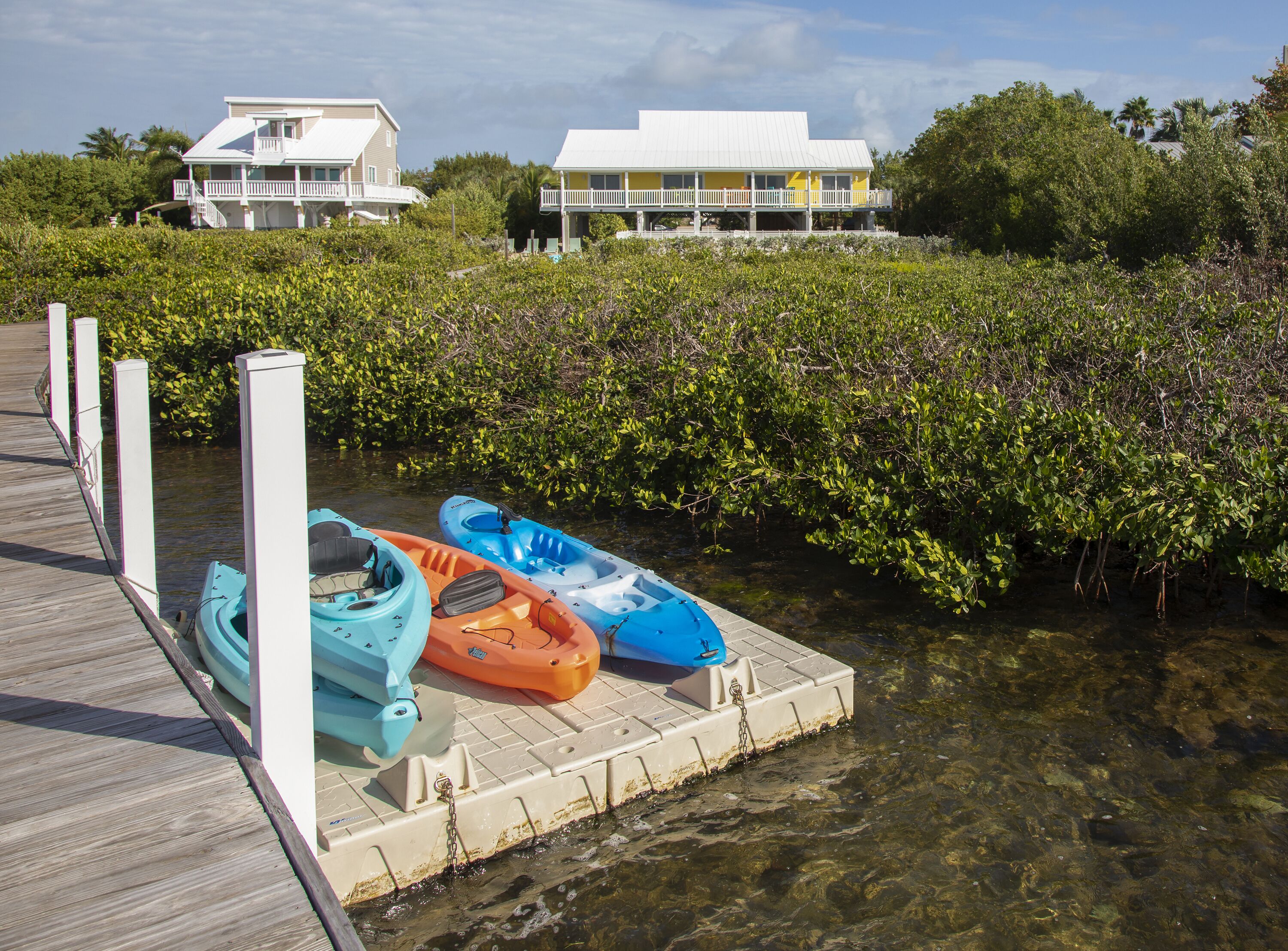 A wooden pier leading to a dock with kayaks and a house in the background.