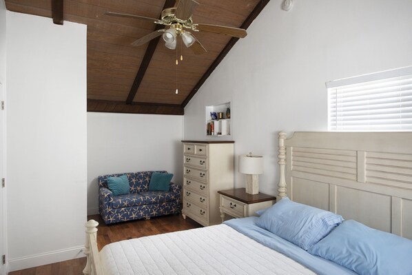 A bedroom with a bed, a dresser, a nightstand, a ceiling fan, a window with blinds, and a blue patterned sofa. - Direct Ocean View! 5 Bed/3 Bath with room for everyone. Large pool and Dock! (Summerland)