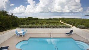 An outdoor swimming pool with lounge chairs and a table, surrounded by a fence, with a view of the sea and greenery. - Direct Ocean View! 5 Bed/3 Bath with room for everyone. Large pool and Dock! (Summerland)