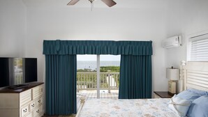 A bedroom with a bed, a TV, a dresser, a nightstand, and a balcony with curtains. - Direct Ocean View! 5 Bed/3 Bath with room for everyone. Large pool and Dock! (Summerland)