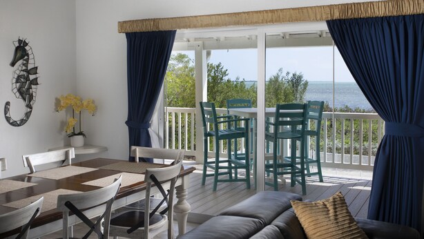 A covered outdoor seating area with a table and chairs, a sofa, and a view of the sea. - Direct Ocean View! 5 Bed/3 Bath with room for everyone. Large pool and Dock! (Summerland)